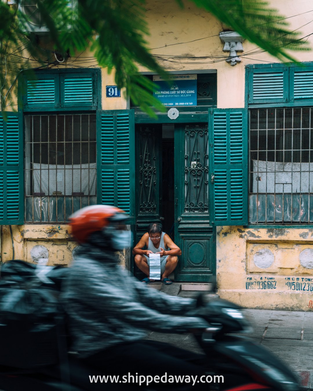 Man reading paper in the early morning at the doors of his house, Hanoi's Old Quarter