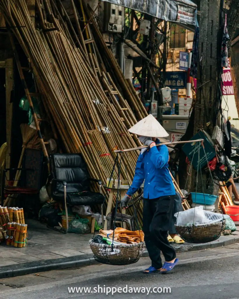 Top Things To Do in Hanoi Old Quarter - Lady carrying goods through a busy woodwork street