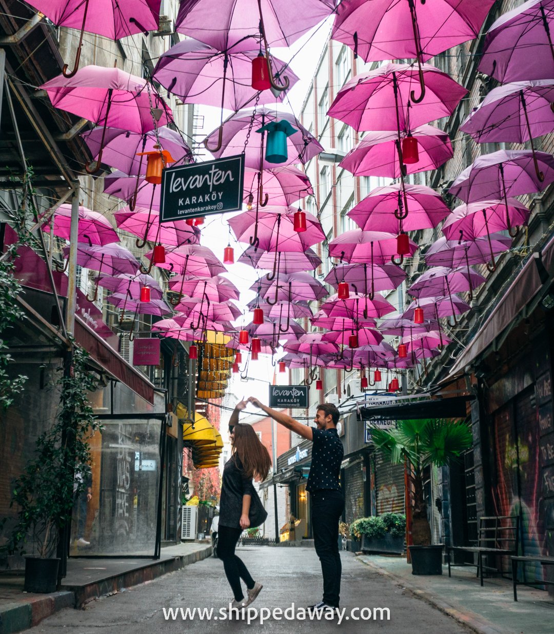 Couple spinning under pink hanging umbrellas, Karakoy, Istanbul