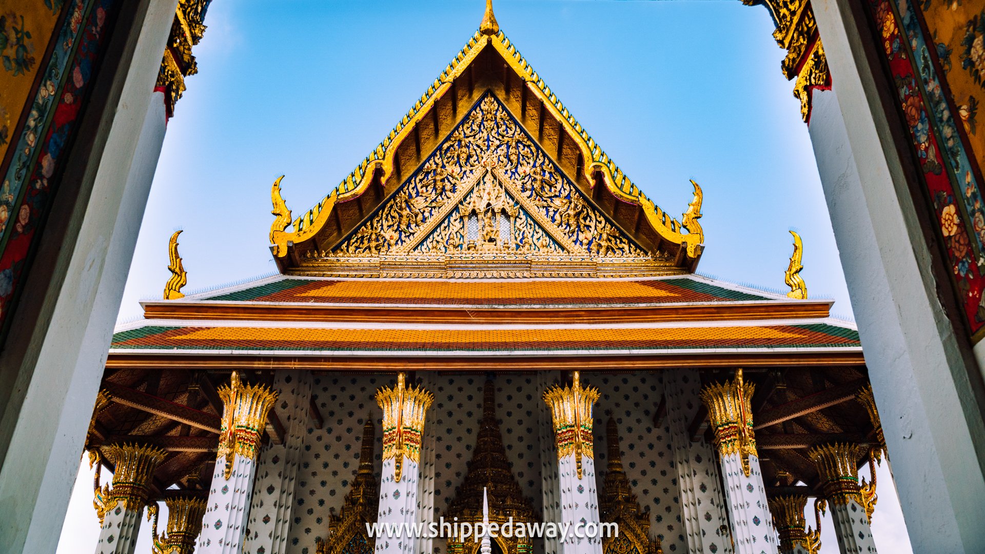 How to visit Wat Arun - Golden gabled roof of the ordination hall at Wat Arun in Bangkok, viewed through a decorative gate with gilded lotus-capital columns.